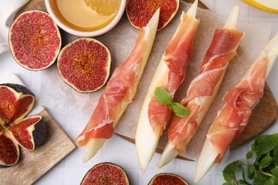 Photo of Tasty melon, jamon and figs served on white tiled table, flat lay