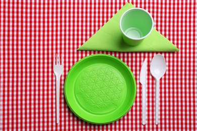 Photo of Table setting with plastic dishware on plaid fabric, flat lay