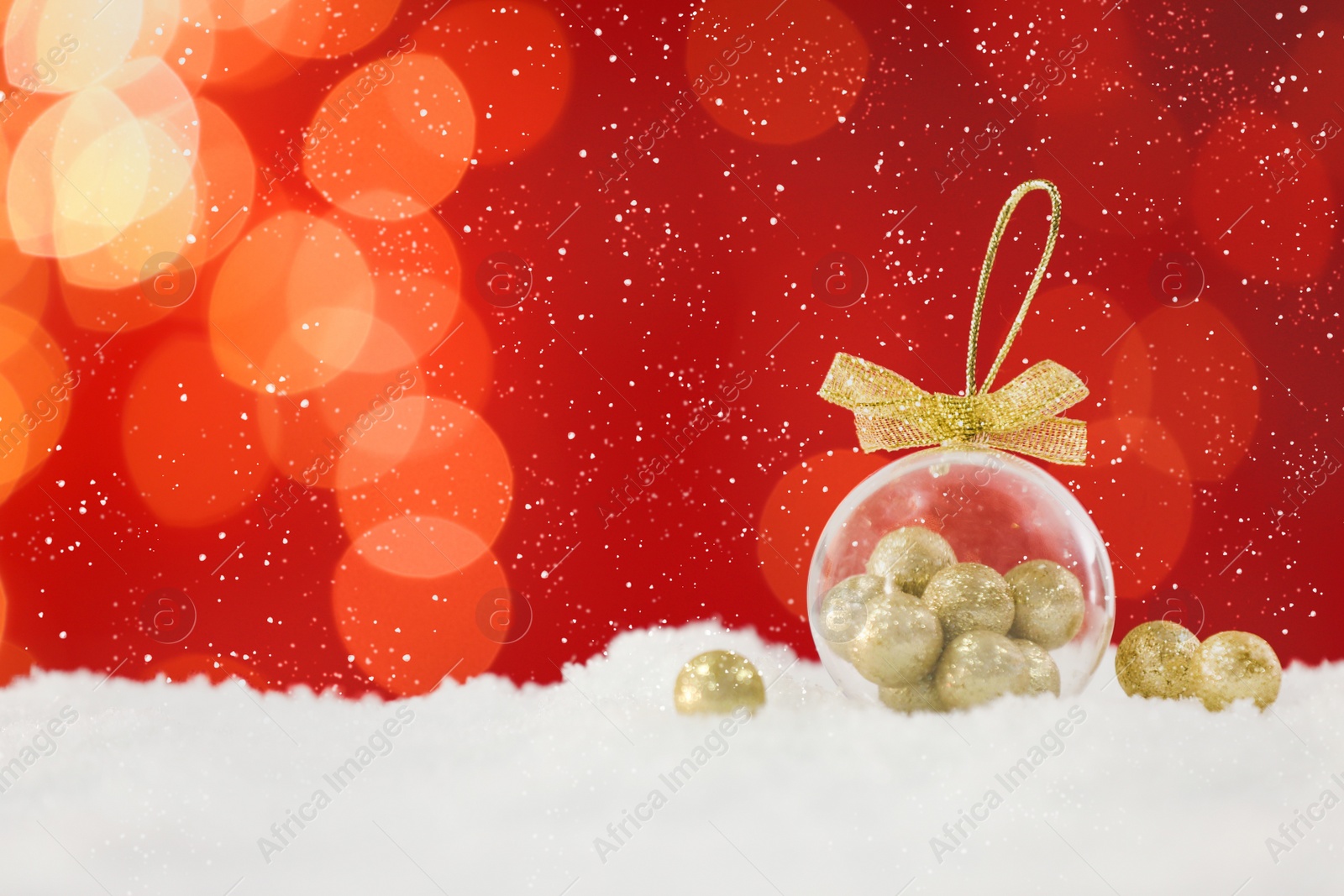 Image of Beautiful transparent Christmas ornament with small golden balls on snow against red background, bokeh effect. Space for text