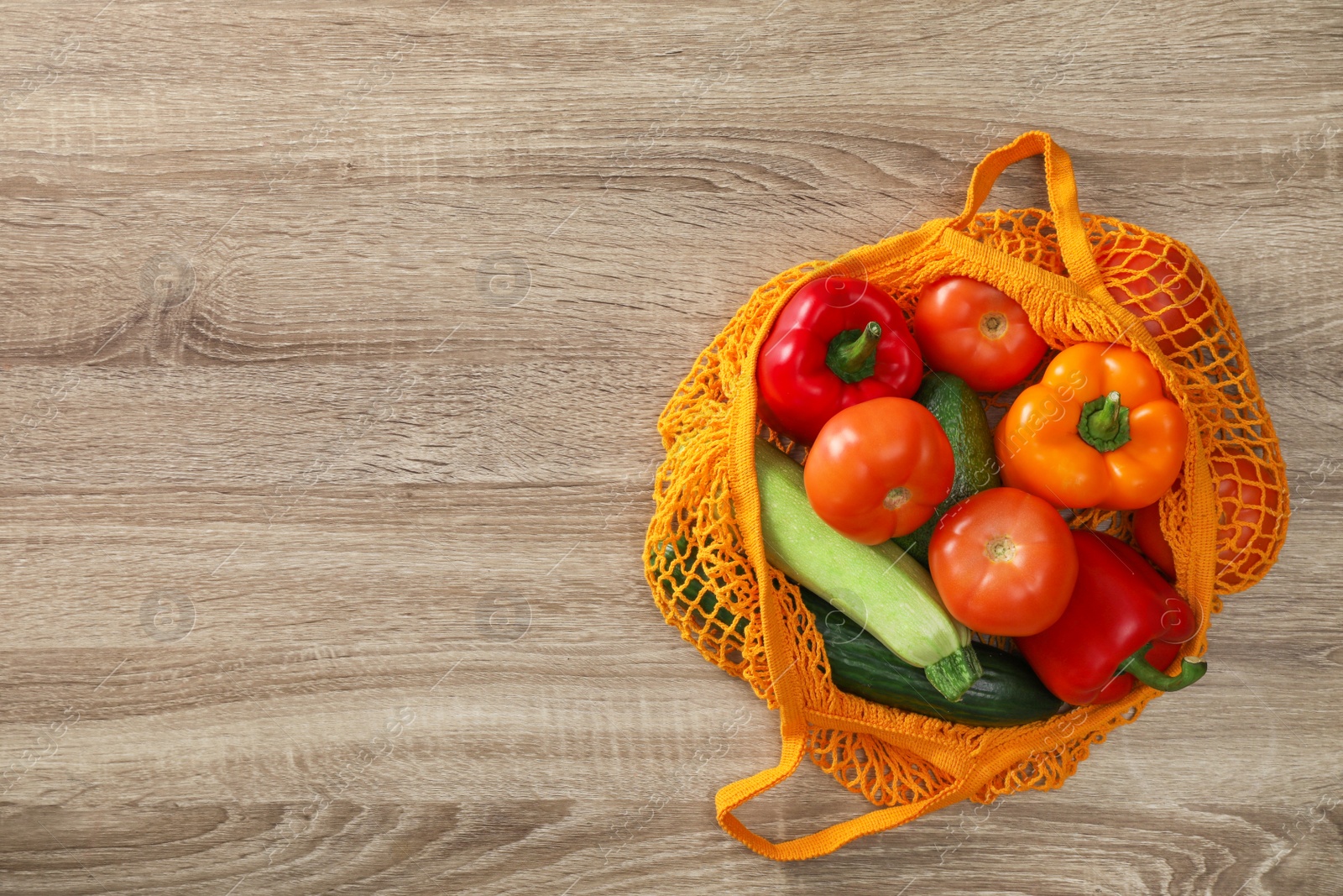 Photo of Net bag with vegetables on wooden table, top view. Space for text