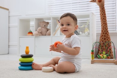 Photo of Cute baby boy playing with toy pyramid on floor at home