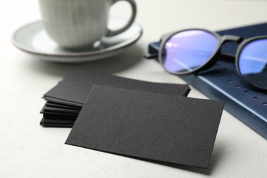 Photo of Blank black business cards, notebook and glasses on white table, closeup. Mockup for design