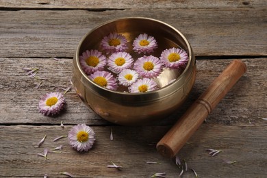 Photo of Tibetan singing bowl with water, chrysanthemum flowers and mallet on wooden table