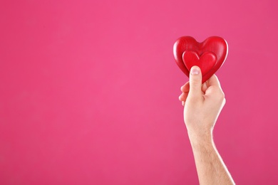 Man holding decorative hearts in hand on color background, space for text