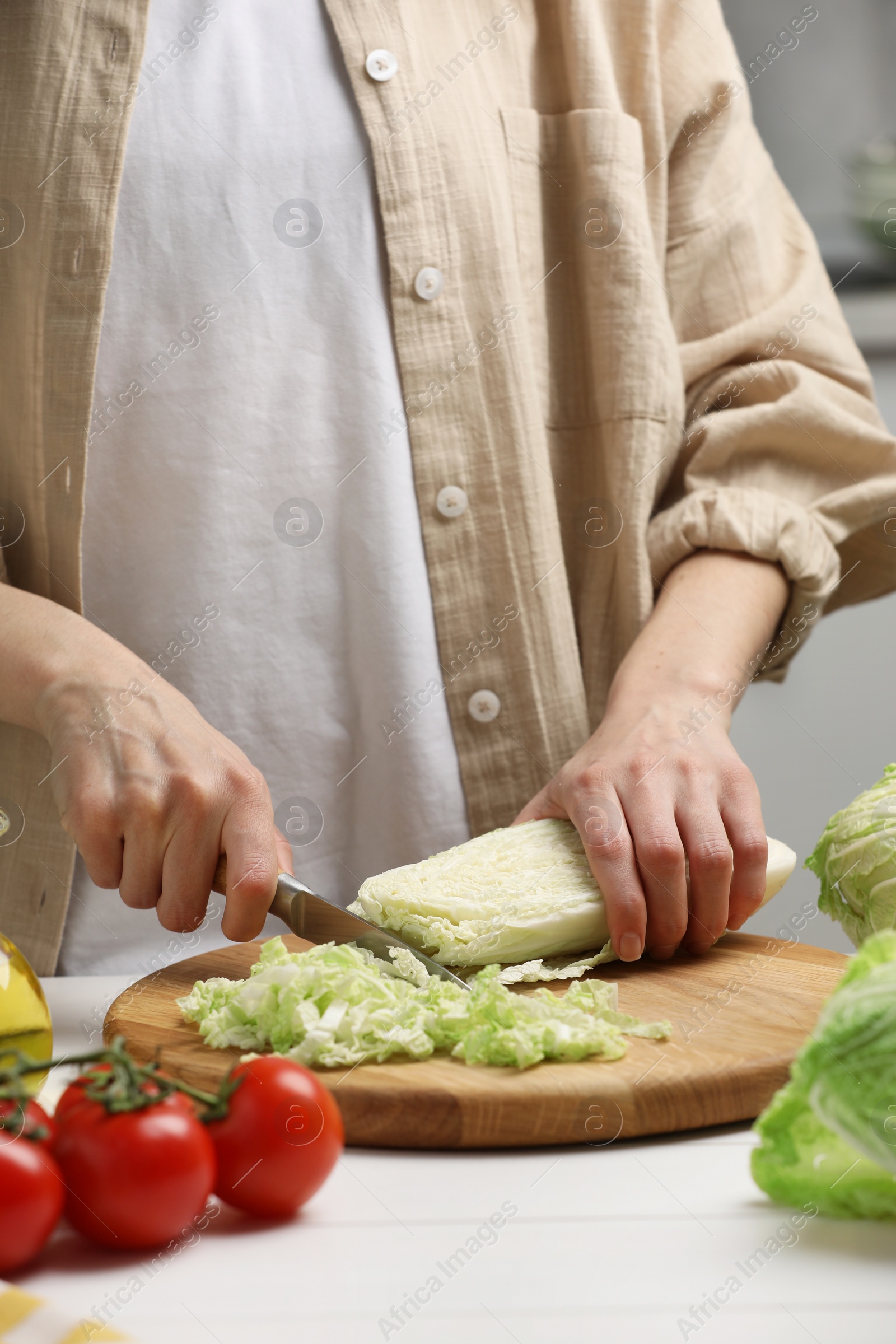 Photo of Woman cutting fresh chinese cabbage at white wooden table in kitchen, closeup