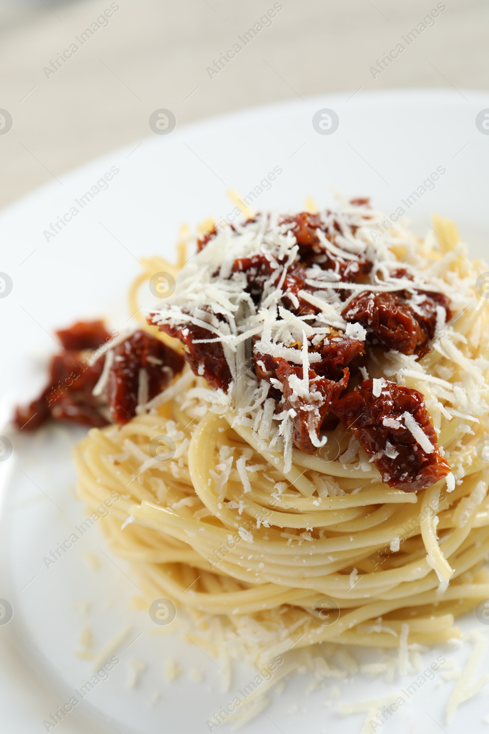 Photo of Tasty spaghetti with sun-dried tomatoes and parmesan cheese on plate, closeup. Exquisite presentation of pasta dish