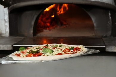 Photo of Putting traditional Italian pizza into oven in restaurant kitchen