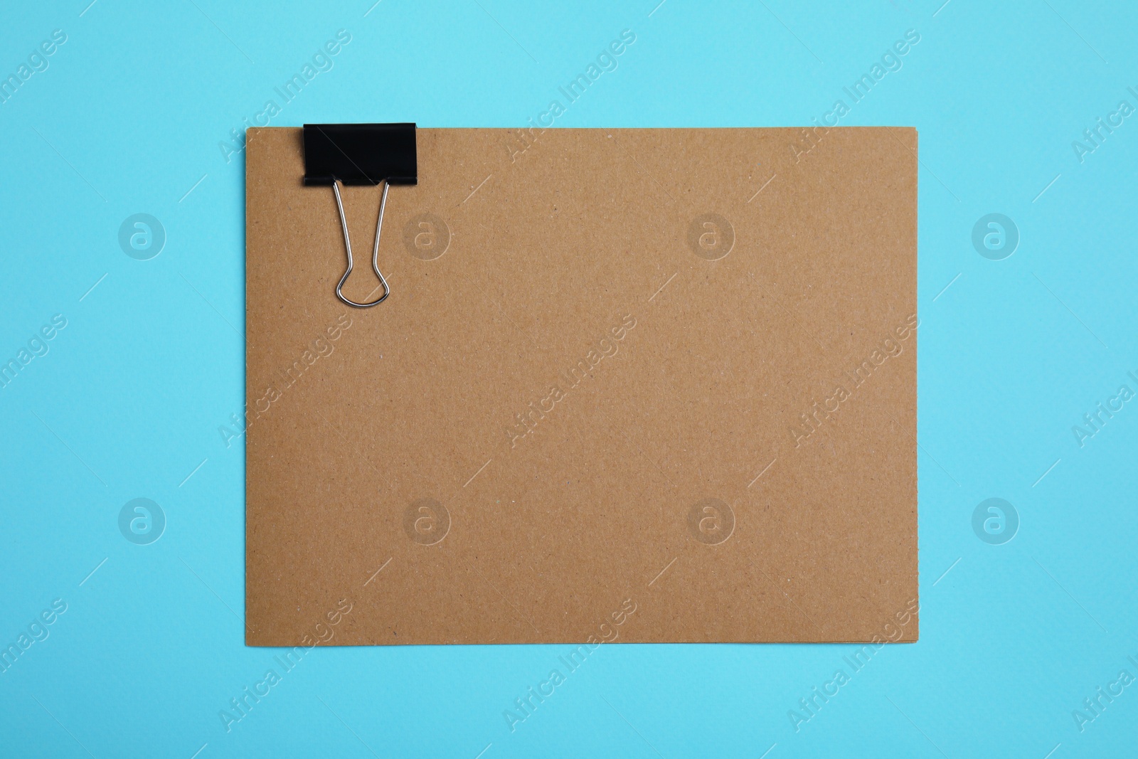 Photo of Sheet of brown paper with clip on light blue background, top view