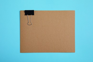 Photo of Sheet of brown paper with clip on light blue background, top view