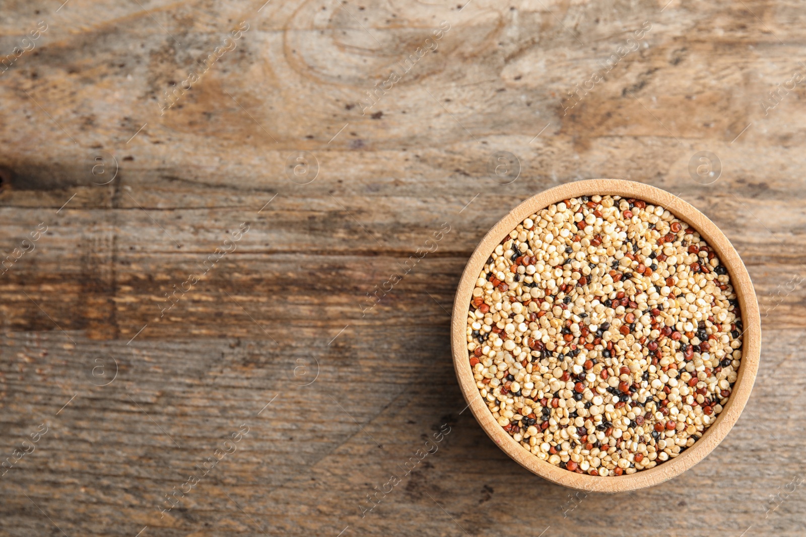 Photo of Bowl with mixed quinoa seeds and space for text on wooden background, top view