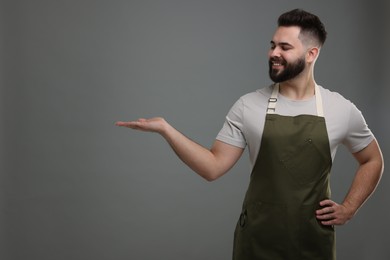 Photo of Smiling man in kitchen apron holding something on grey background. Mockup for design