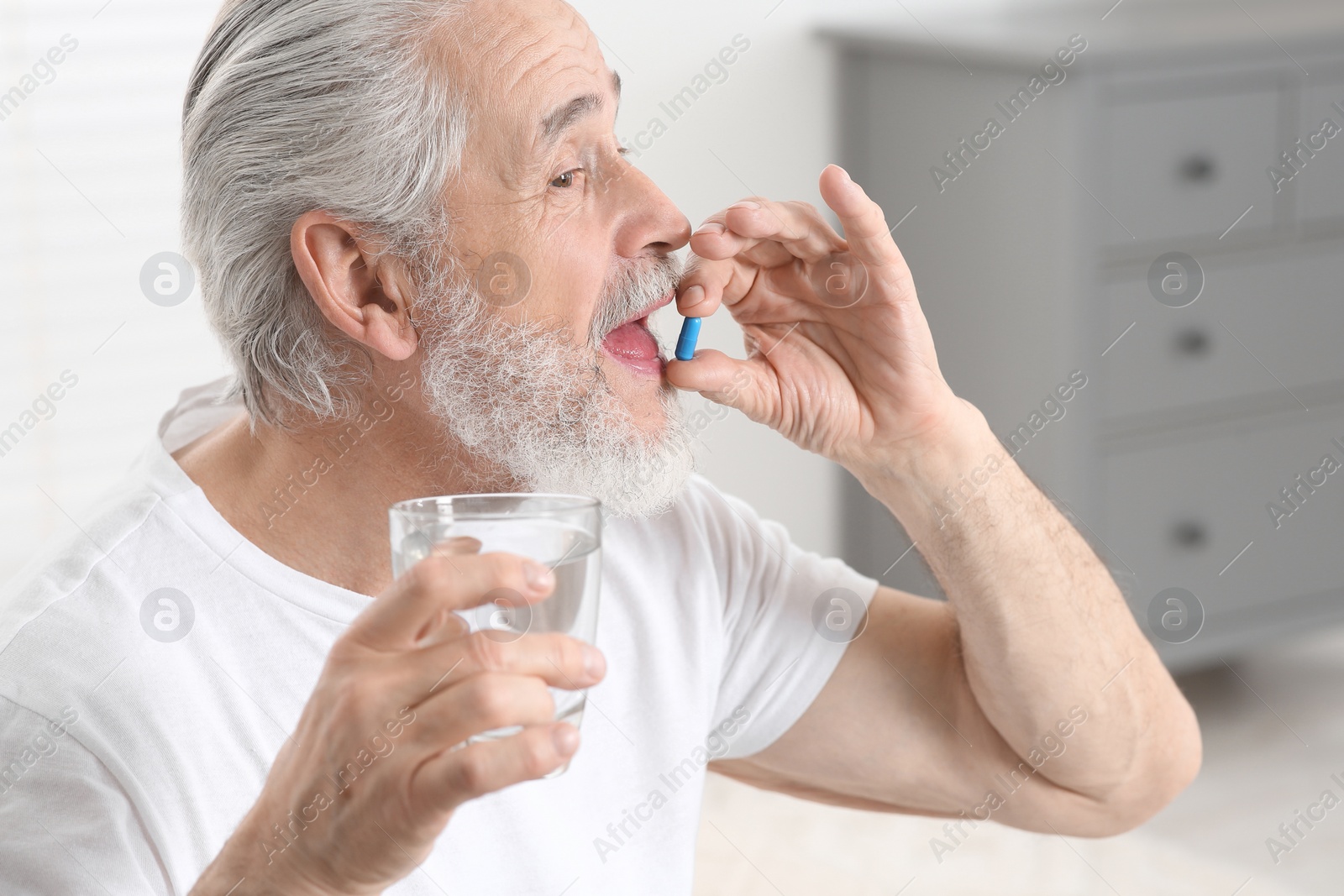 Photo of Senior man with glass of water taking pill indoors