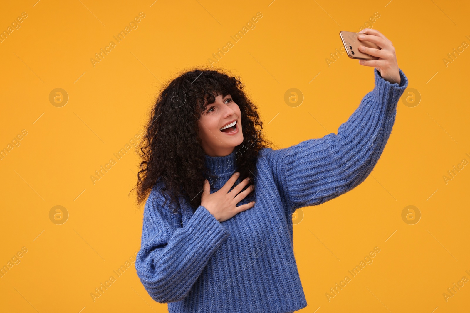 Photo of Beautiful young woman taking selfie with smartphone on orange background