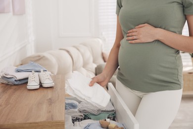 Photo of Pregnant woman holding diapers at home, closeup