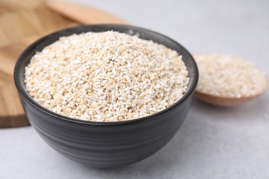 Photo of Dry barley groats in bowl on light grey table, closeup
