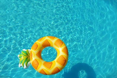 Photo of Bright inflatable pineapple ring floating in swimming pool on sunny day, above view