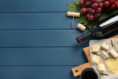 Tasty red wine and snacks on blue wooden table, flat lay. Space for text