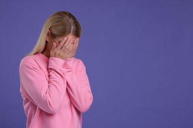Photo of Resentful woman covering face on purple background. Space for text