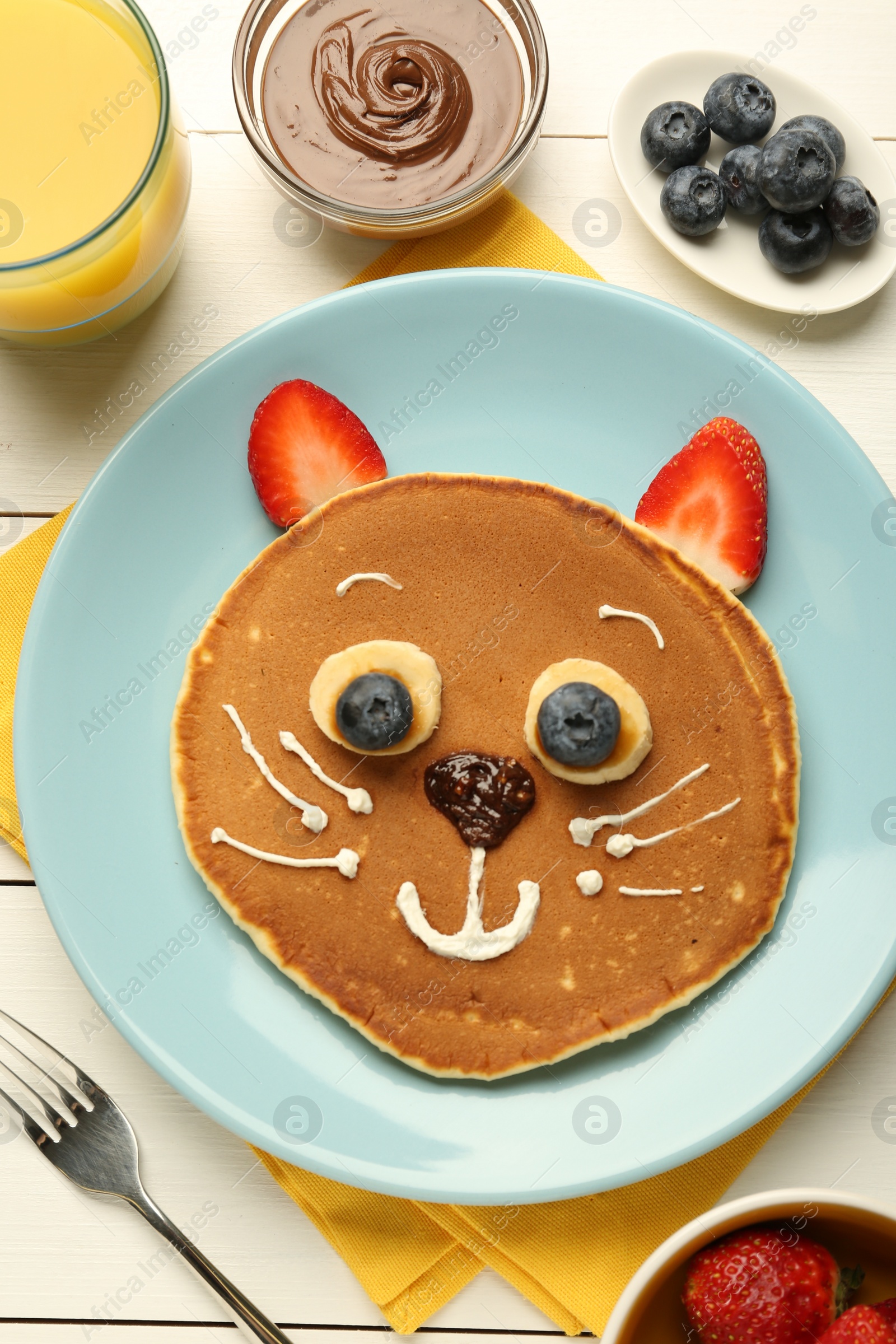 Photo of Creative serving for kids. Plate with cute cat made of pancakes, berries, cream, banana and chocolate paste on white wooden table, flat lay