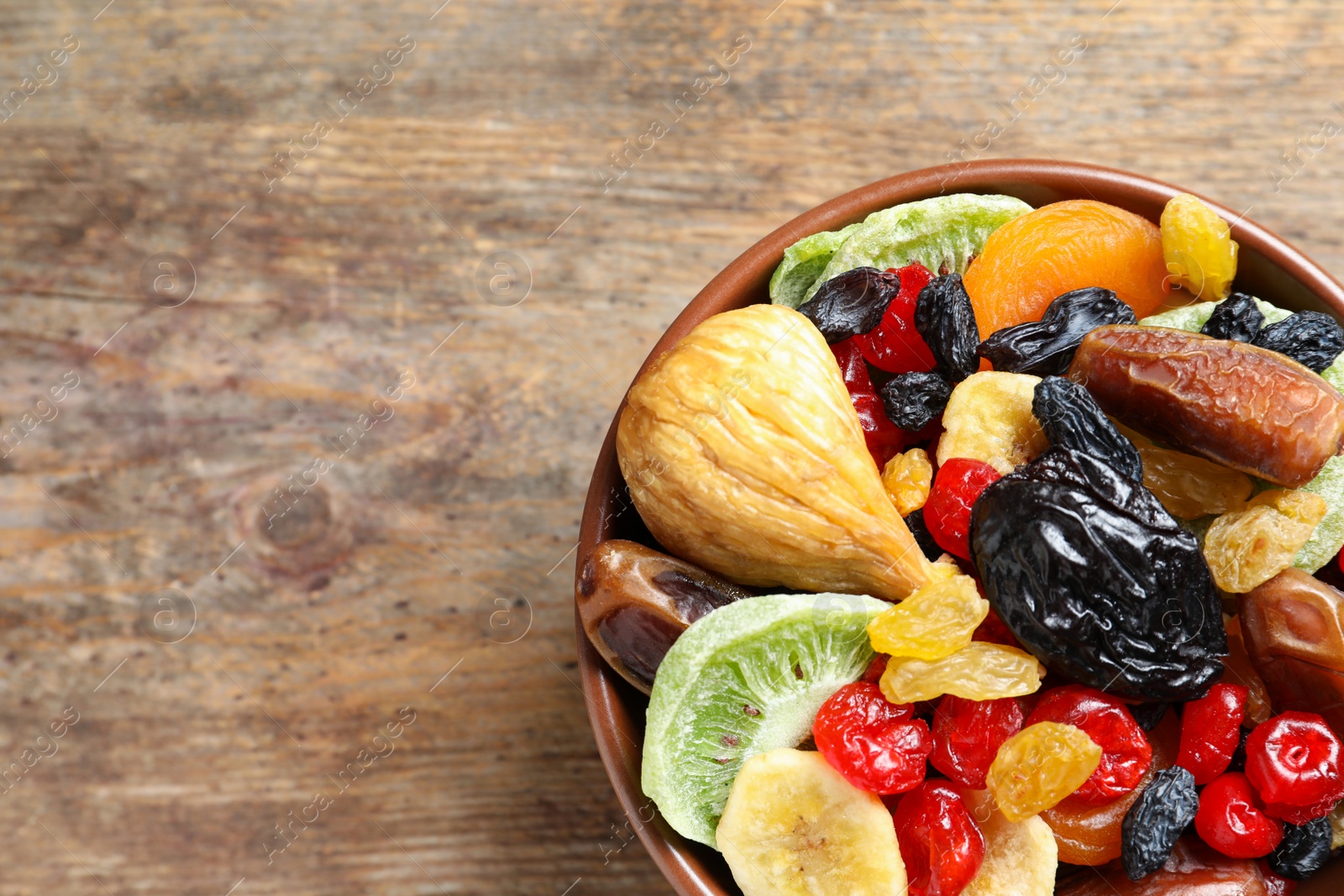 Photo of Bowl of different dried fruits on wooden background, top view with space for text. Healthy lifestyle