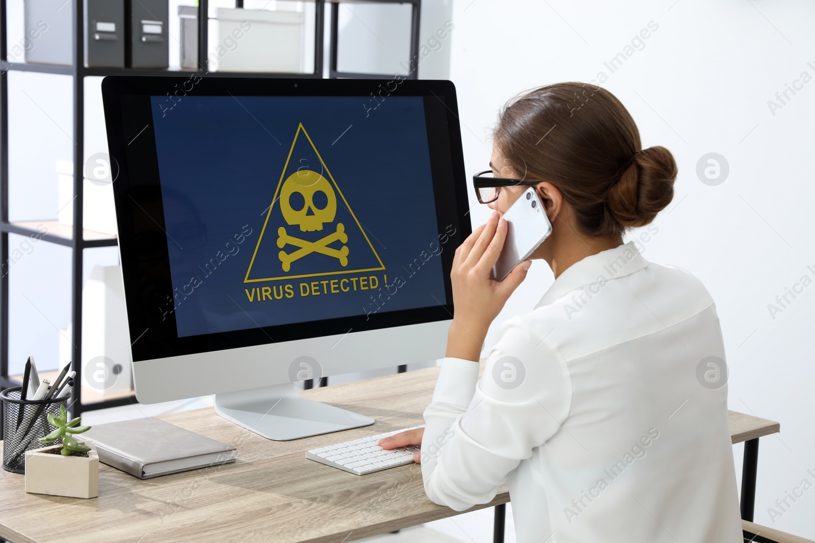 Photo of Office worker in front of computer with warning about virus attack on screen