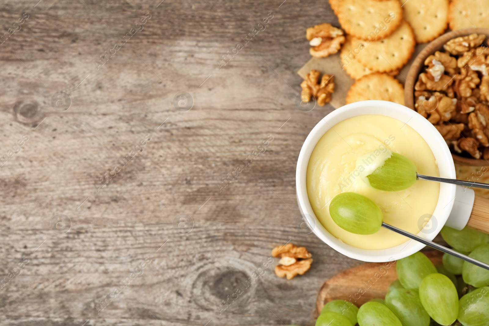 Photo of Dipping grapes into fondue pot with white chocolate on wooden table, top view. Space for text