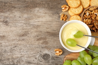 Dipping grapes into fondue pot with white chocolate on wooden table, top view. Space for text