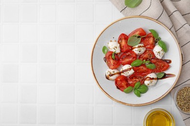 Photo of Tasty salad Caprese with mozarella balls, tomatoes, basil and other ingredients on white tiled table, flat lay. Space for text