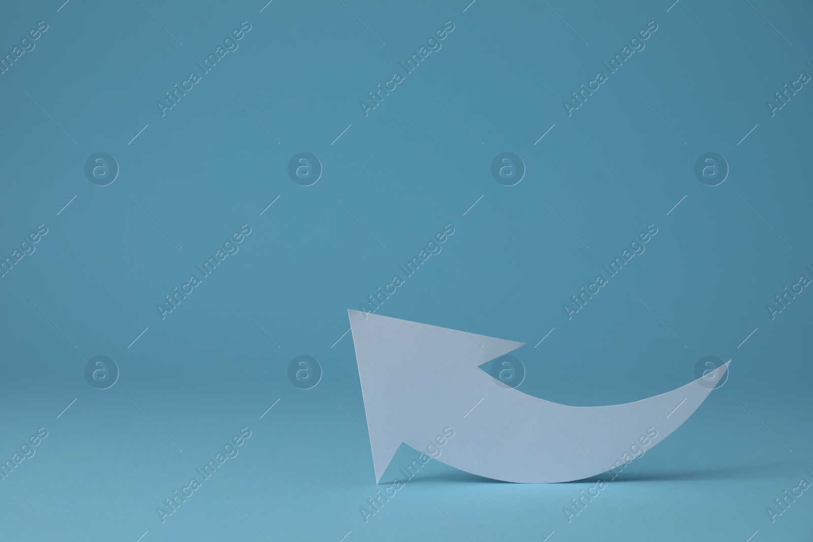 Photo of White curved paper arrow on light blue background, space for text