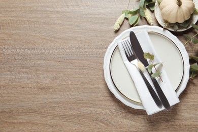 Festive table setting with floral decor and pumpkins  on wooden background, flat lay. Space for text