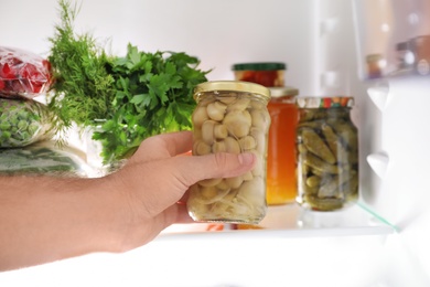 Man taking jar with mushrooms out of refrigerator in kitchen, closeup