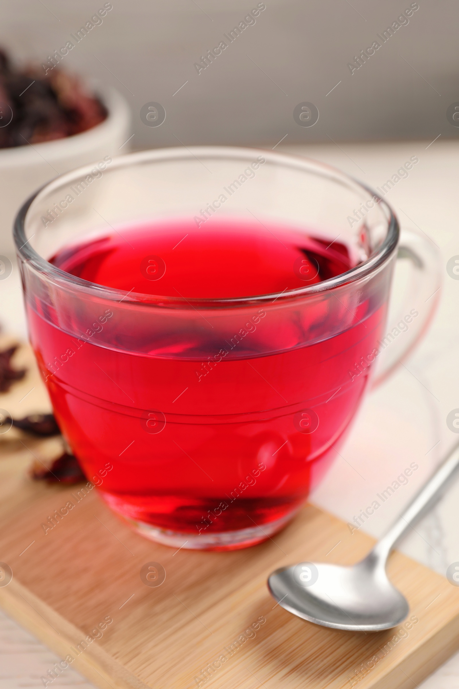 Photo of Cup of fresh hibiscus tea and spoon on wooden board, closeup