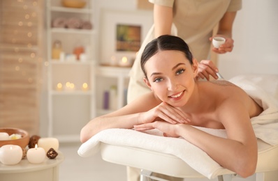 Beautiful young woman having massage with body scrub in spa salon