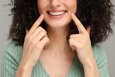Photo of Young woman showing her teeth with whitening strip on grey background, closeup