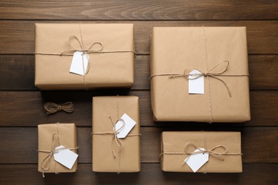 Photo of Parcels wrapped in kraft paper with tags on wooden table, flat lay