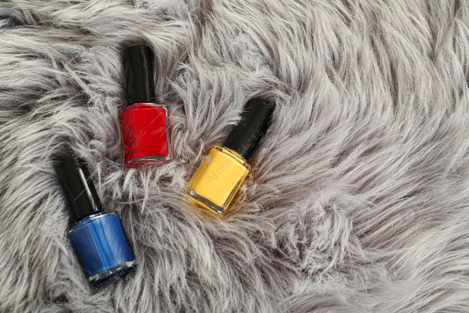 Photo of Bright nail polishes in bottles on grey faux fur, top view. Space for text