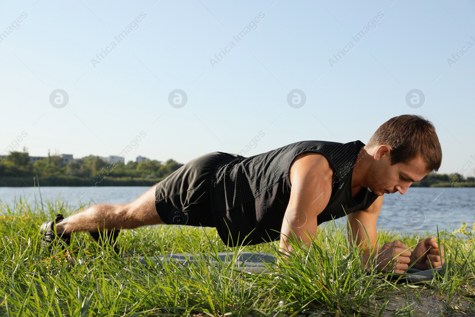 Photo of Sporty man doing plank exercise on green grass near river