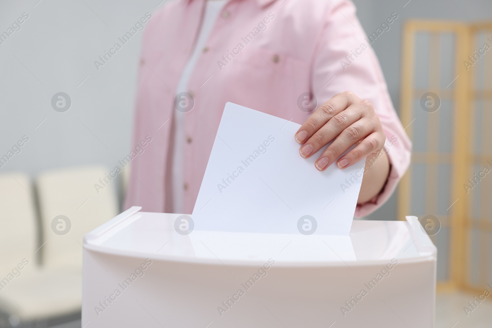 Photo of Woman putting her vote into ballot box on blurred background, closeup