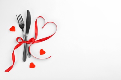 Photo of Beautiful cutlery set, hearts and red ribbon on white background, flat lay with space for text. Valentine's Day dinner