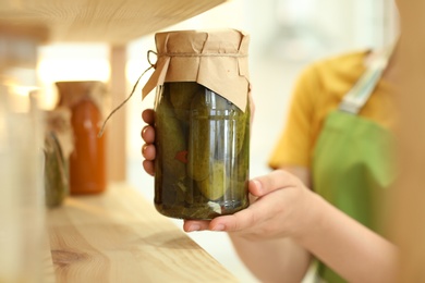 Photo of Woman putting jar of pickles on shelf indoors, closeup