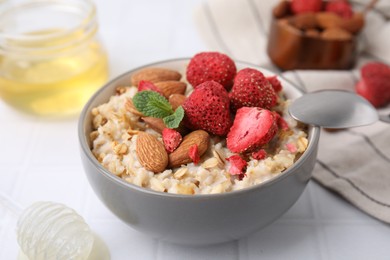 Delicious oatmeal with freeze dried strawberries, almonds and mint on white tiled table, closeup