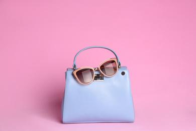 Photo of Stylish woman's bag and sunglasses on light pink background
