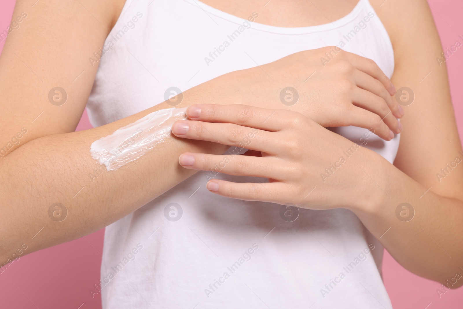 Photo of Young woman applying body cream onto arm on pink background, closeup