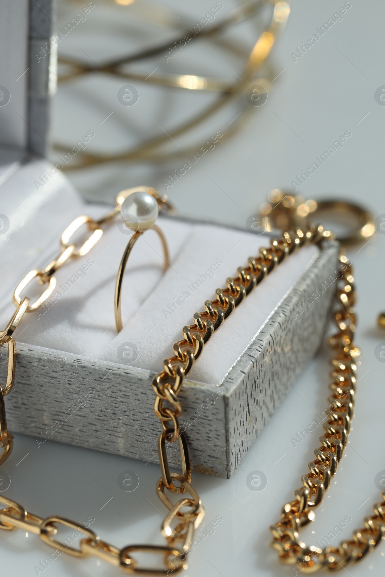 Photo of Metal chain and jewelry box with ring on white table, closeup