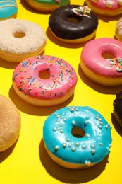 Photo of Different delicious glazed doughnuts on yellow background