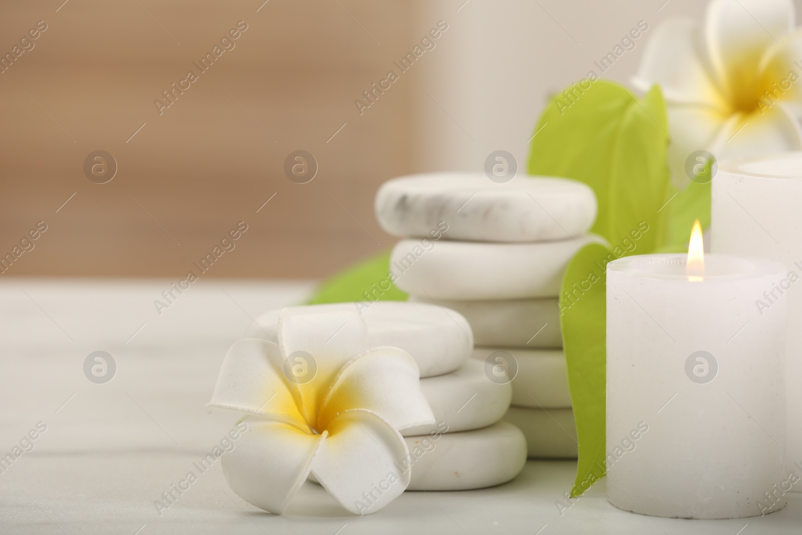 Photo of Spa composition. Burning candle, plumeria flowers, stones and green leaves on white table, closeup. Space for text