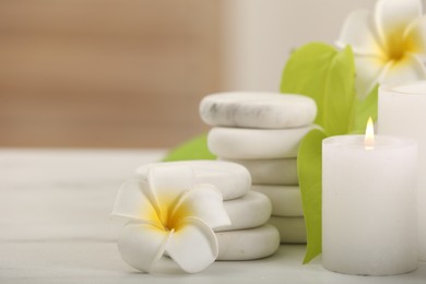 Spa composition. Burning candle, plumeria flowers, stones and green leaves on white table, closeup. Space for text