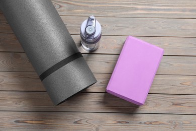 Exercise mat, yoga block and bottle of water on wooden floor, flat lay