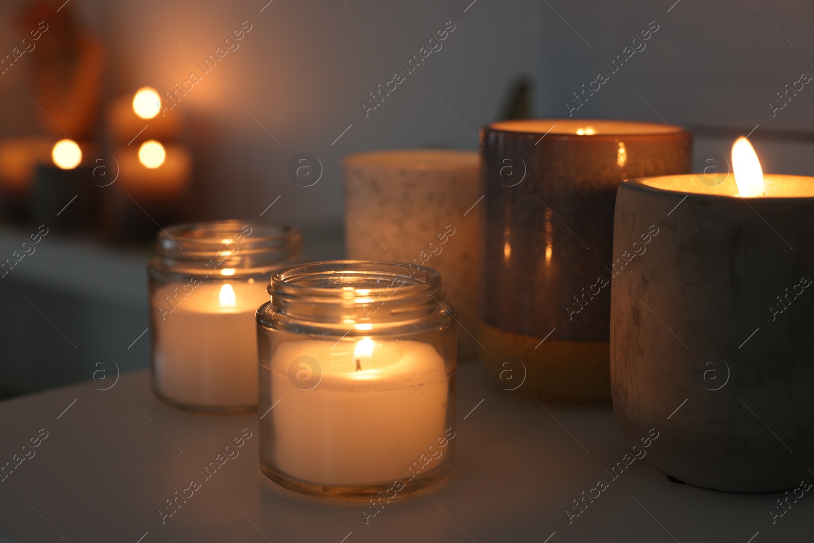 Photo of Burning wax candles on white table in room, closeup