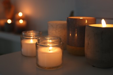 Burning wax candles on white table in room, closeup
